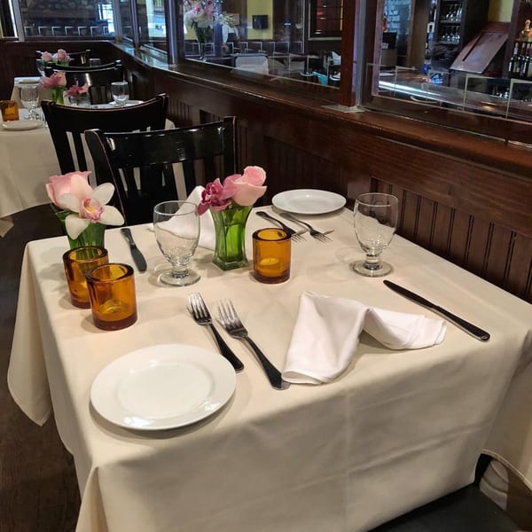 A set table at Da Nicola, with white tablecloths, plates, silverware, and pink flowers.