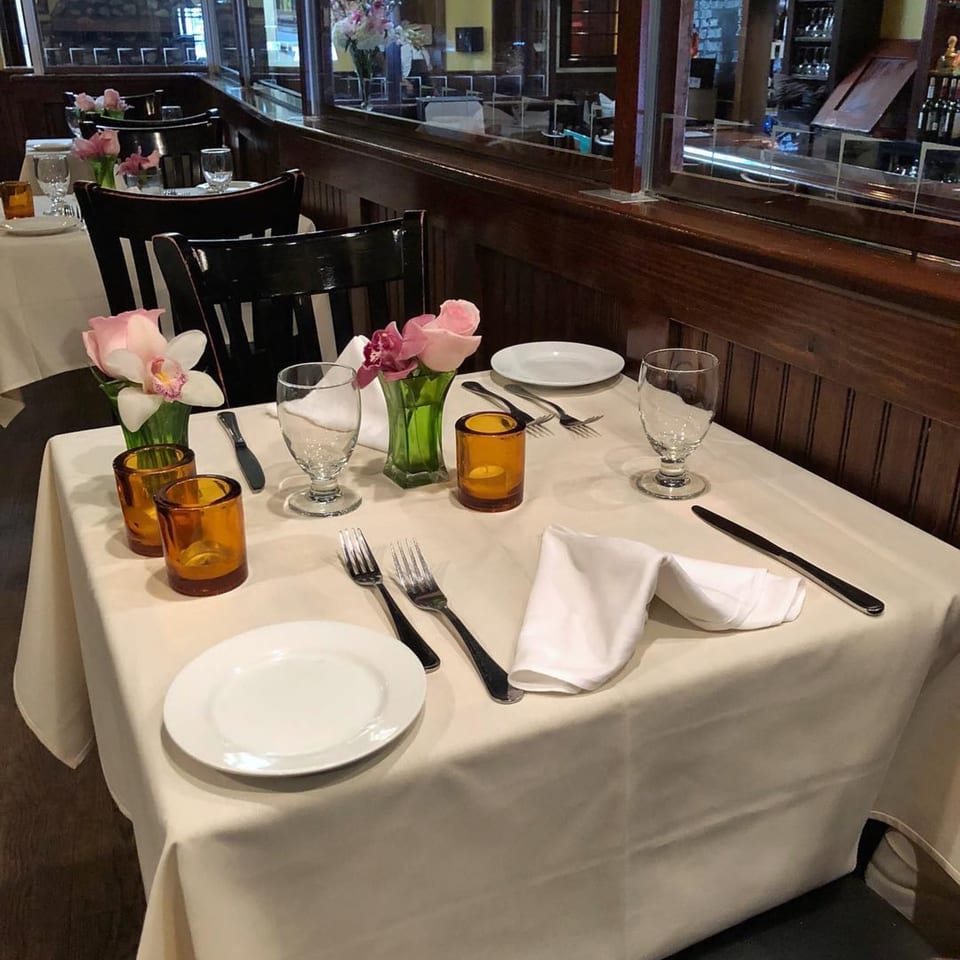 A set table at Da Nicola, with white tablecloths, plates, silverware, and pink flowers.
