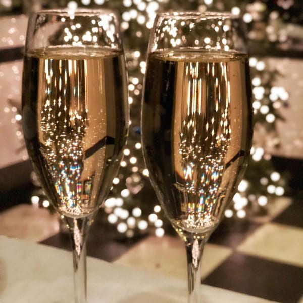 Two champagne flutes with reflections of sparkling lights, set against a blurred festive background.