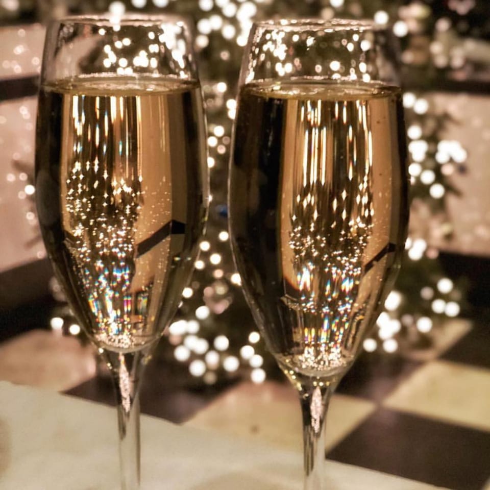 Two champagne flutes with reflections of sparkling lights, set against a blurred festive background.
