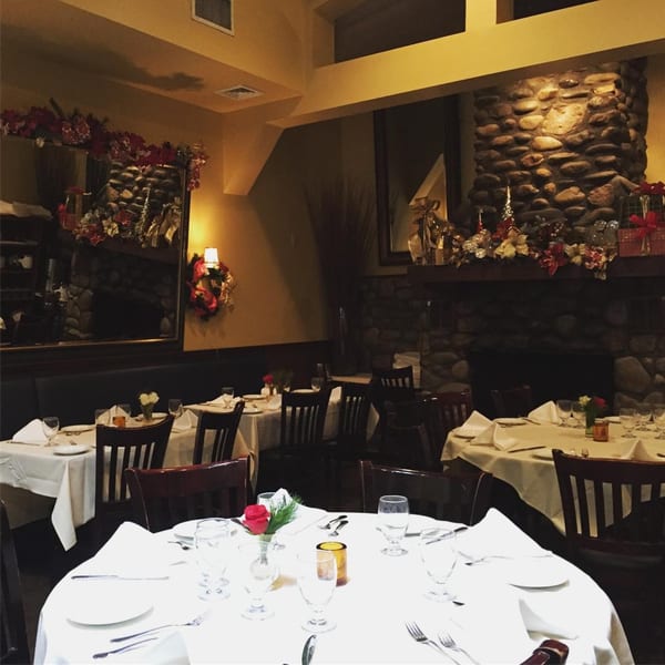 An Italian restaurant dining room with tables set with white tablecloths and holiday decorations.