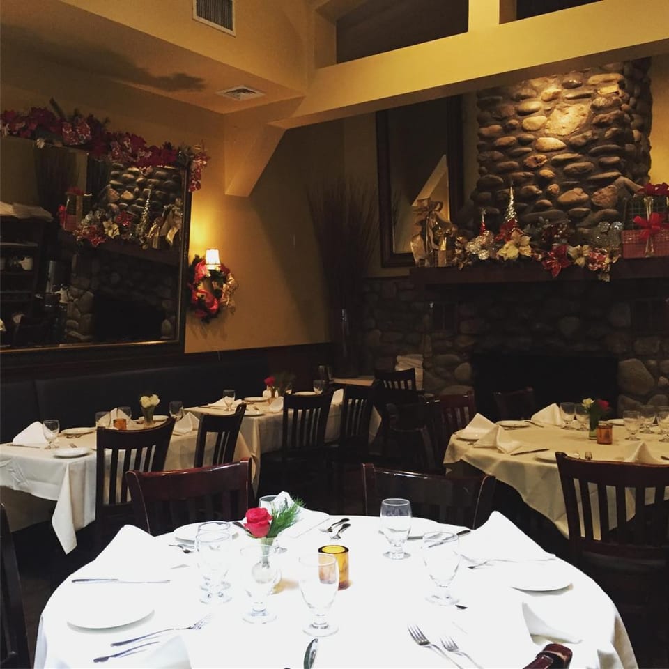 An Italian restaurant dining room with tables set with white tablecloths and holiday decorations.