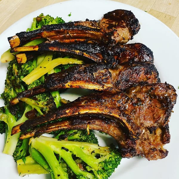 Grilled lamb chops with a dark glaze, served over bright green broccoli florets on a white plate.