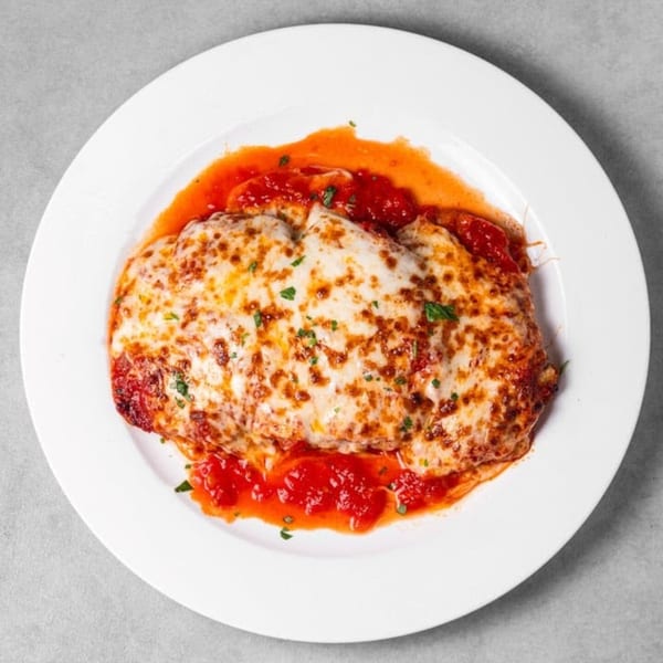 Da Nicola's chicken parmesan, topped with melted mozzarella cheese and red sauce, on a white plate.